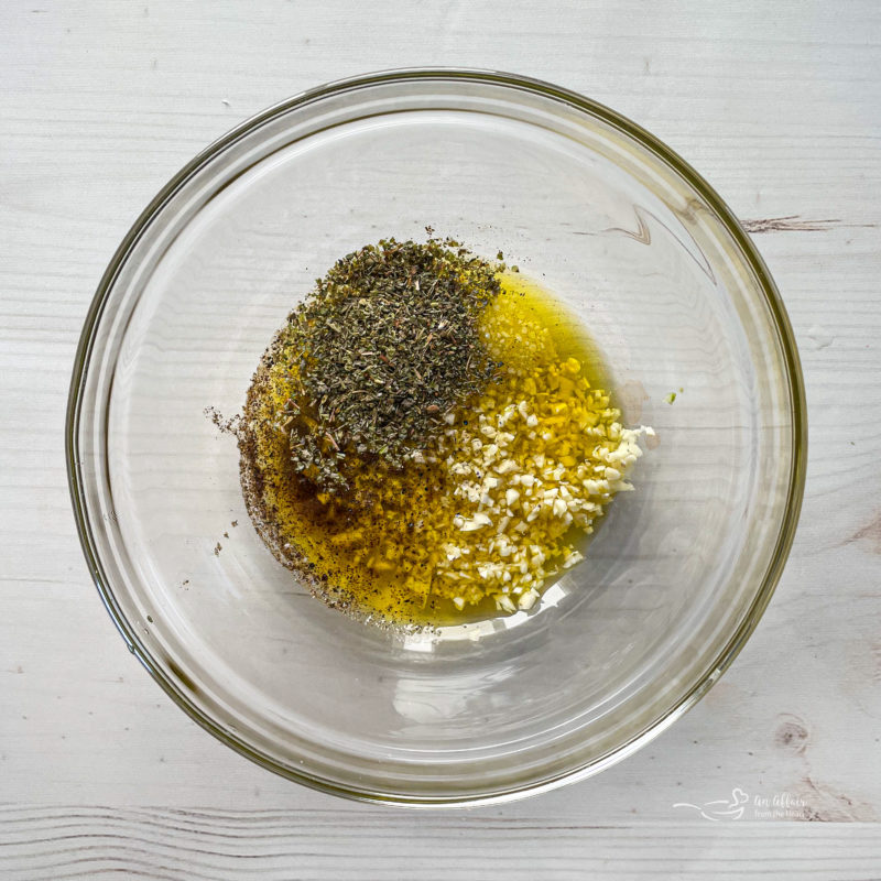 Top view of garlic, olive oil, and seasoning in clear bowl