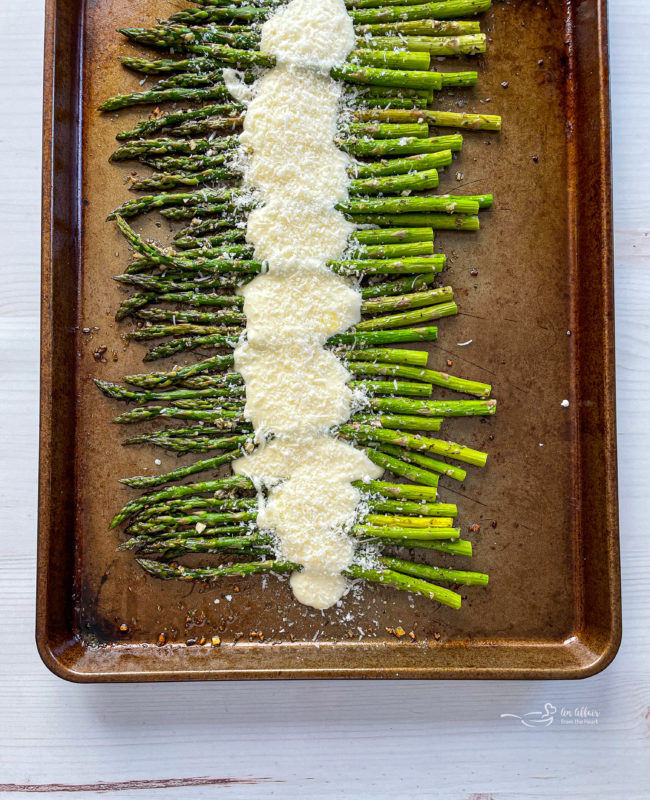 Top view of asparagus on baking sheet with cheese sauce