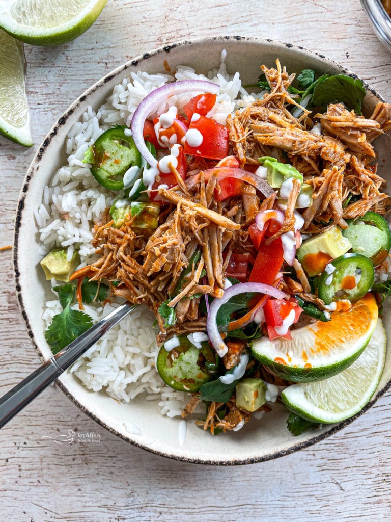 One bowl of cilantro lime pork with limes, tomatoes, onions, rice, and jajapeños