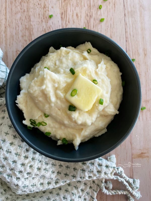 Top view of mashed potatoes in black bowl with chives and butter