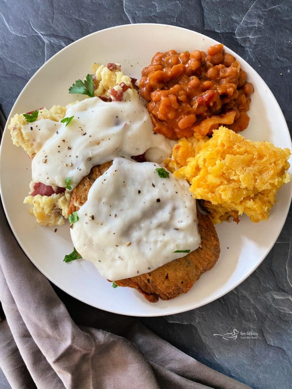 Plate of chicken patties and mashed potatoes with gravy, beans, and corn pie pudding