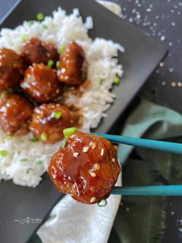 Sticky Asian Meatballson rice with chopsticks holding one meatball