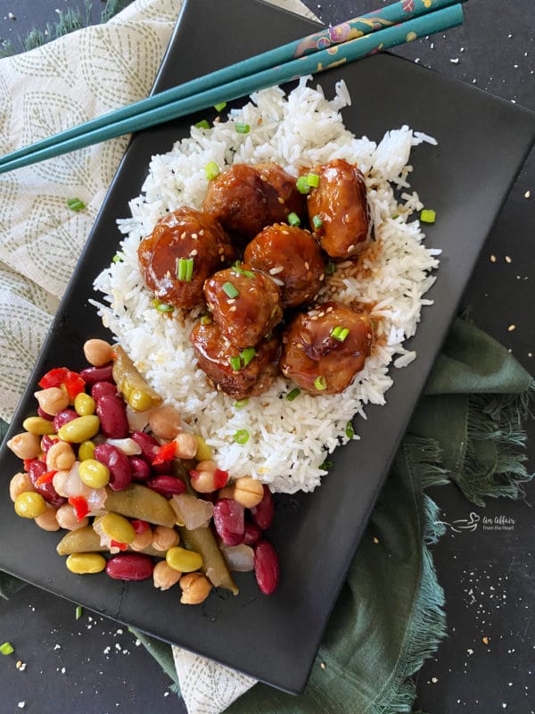 Sticky Asian Meatballs on black plate over rice with bean salad