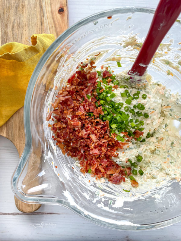 cream cheese, bacon, and green onions being stirred in glass bowl