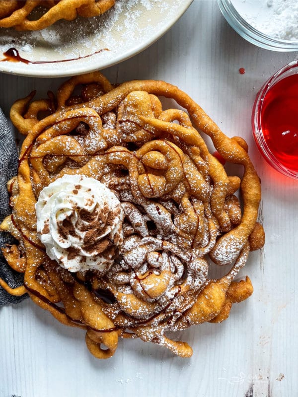 top view of funnel cake on white surface with whipped cream and drizzled chocolate