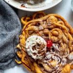 funnel cake with cherry and whipped cream drizzled with chocolate sauce