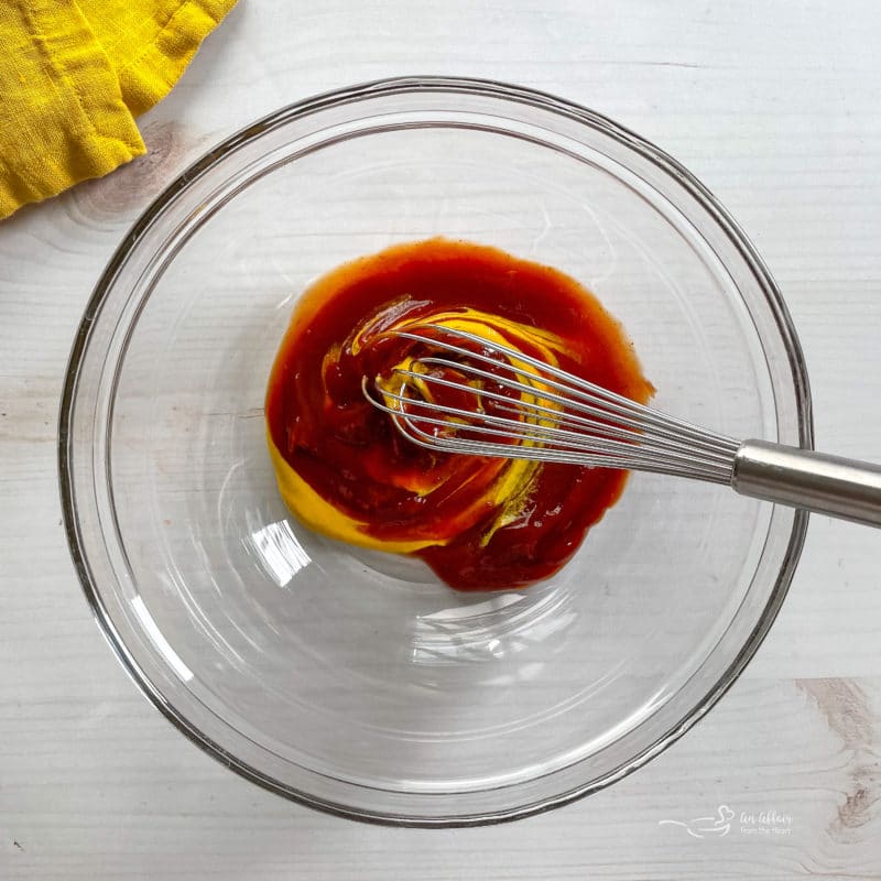 whisking ketchup and mustard in bowl with whisk