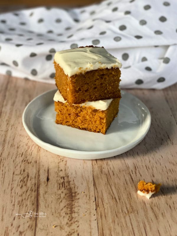 two carrot cake bars on white plate with cream cheese frosting