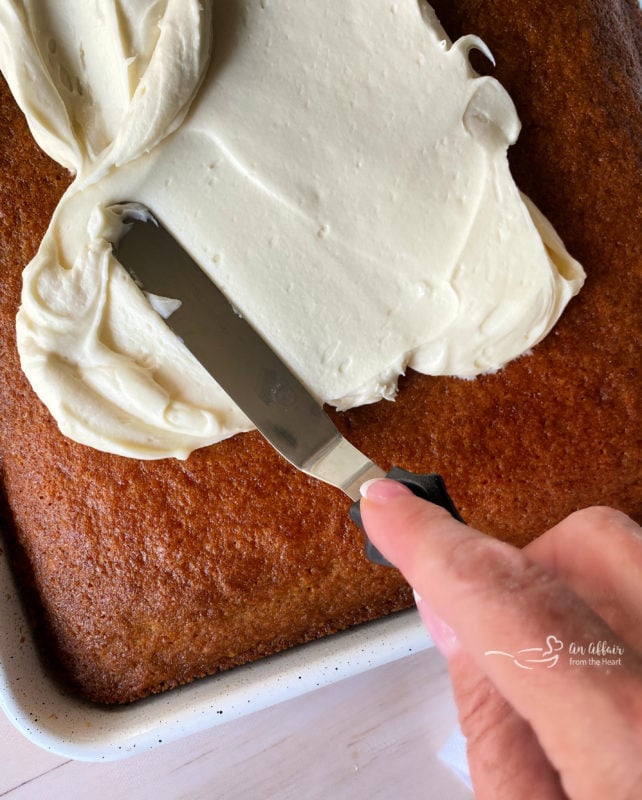 spreading cream cheese frosting on cooled carrot cake with baking tool