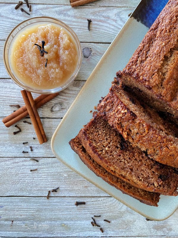 one loaf of applesauce bread on plate with bowl of applesauce and cinnamon sticks