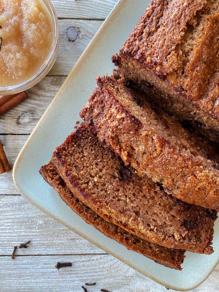 one loaf of applesauce bread on white plate with applesauce in bowl