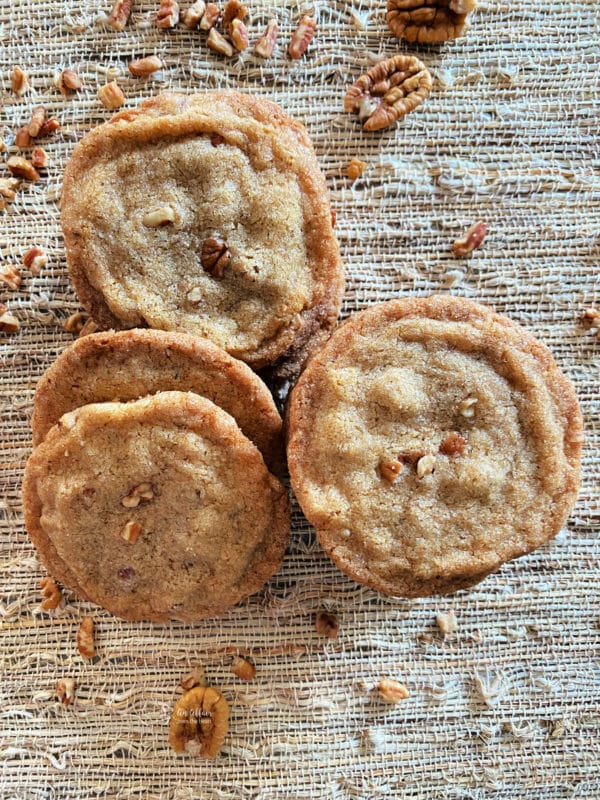 top view of pecan butter cookies on tan surface with pecans
