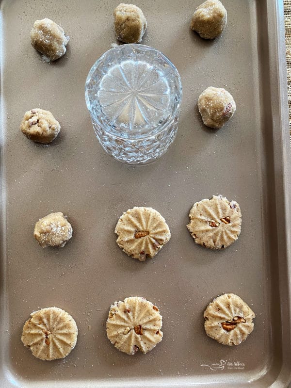 pecan butter cookie dough on baking sheet with designs, glass, and pecans