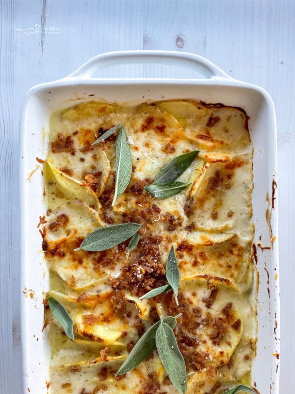 top view of potatoes au gratin in baking dish with bacon and sage leaves