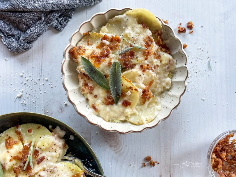 two bowls of the best potatoes au gratin recipe from scratch topped with sage and bacon