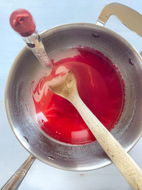 cinnamon, water, corn syrup, sugar, and food coloring in saucepan with thermometer 