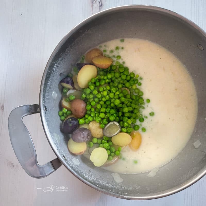 pot filled with white sauce, peas, and potatoes