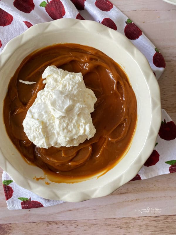 spreading cream cheese on caramel dip in pie plate