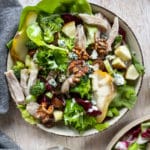 one bowl of salad with broccoli, lettuce, chicken, grapes, walnuts, pears, dressing