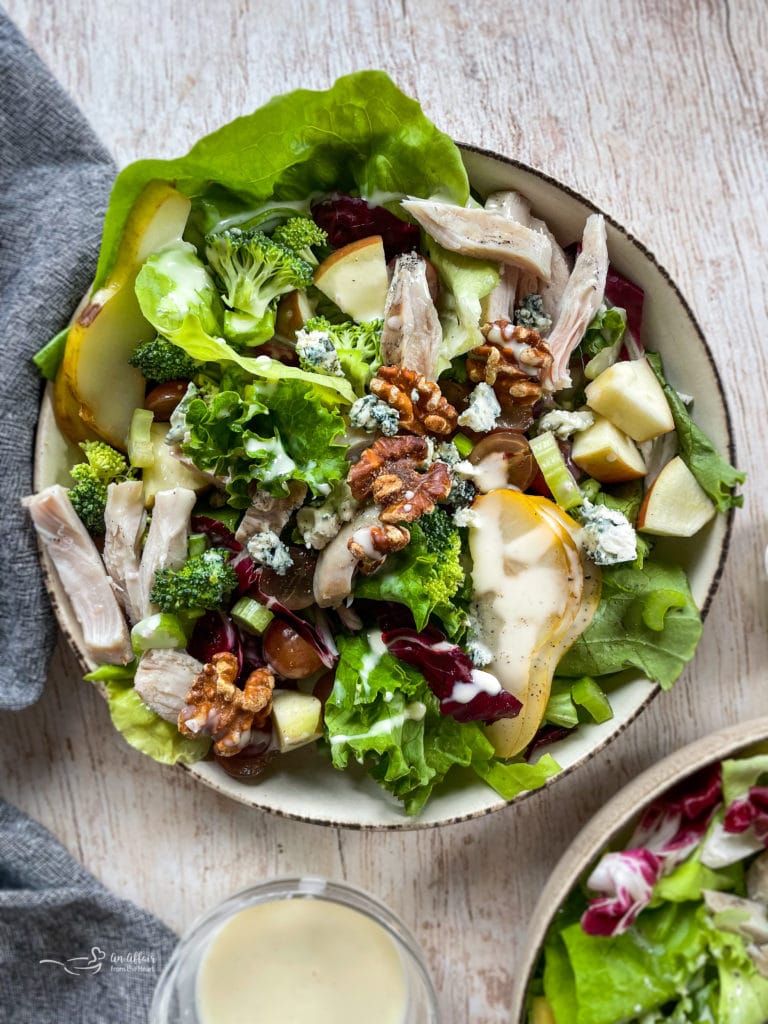 one bowl of salad with broccoli, lettuce, chicken, grapes, walnuts, pears, dressing