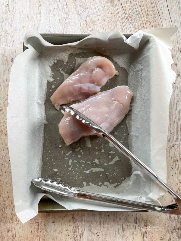 raw chicken on pan with tongs