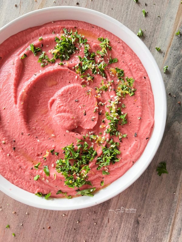white bowl with pink hummus and parsley