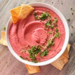 white bowl with pink hummus and parsley with chips
