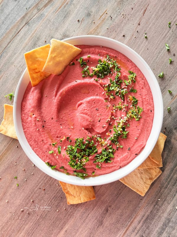 white bowl with pink hummus and parsley with chips