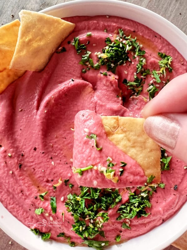 white bowl of pink hummus with crackers and parsley