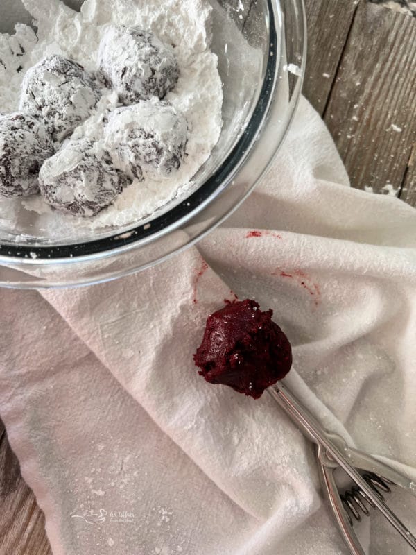 rolling red velvet cookie dough in bowl of powdered sugar