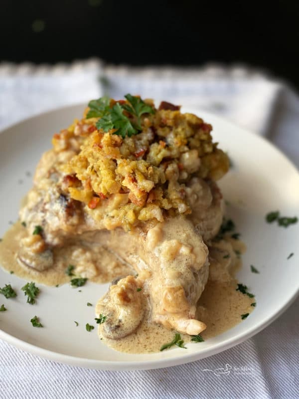 one white plate with baked pork chop with stuffing with gravy and herbs