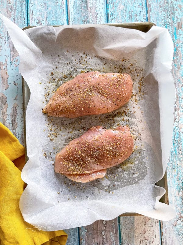 two chicken breasts on baking sheet with lemon pepper seasoning