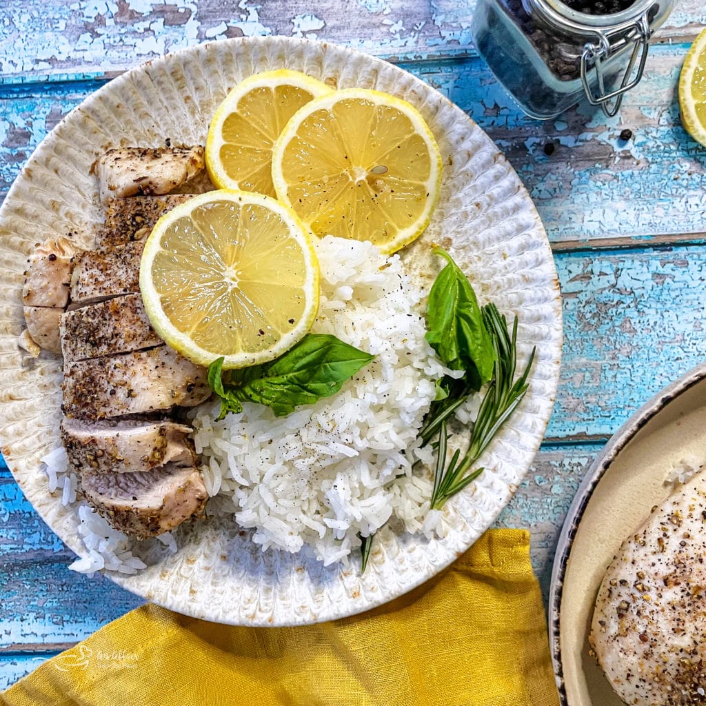 one white plate with lemon pepper chicken, rice, lemon wheels, and basil