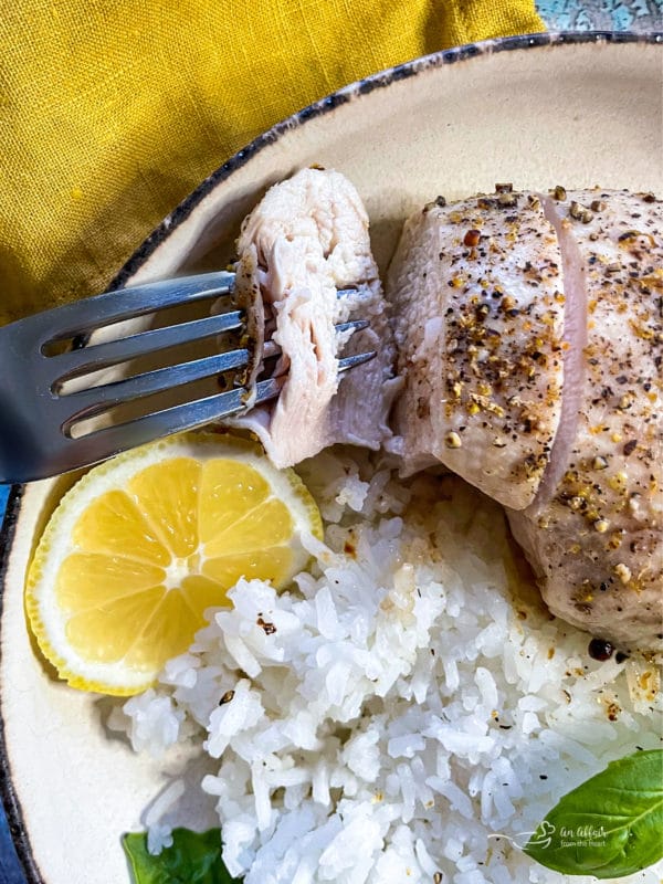 one plate of lemon pepper chicken with fork, lemon, and rice with basil 