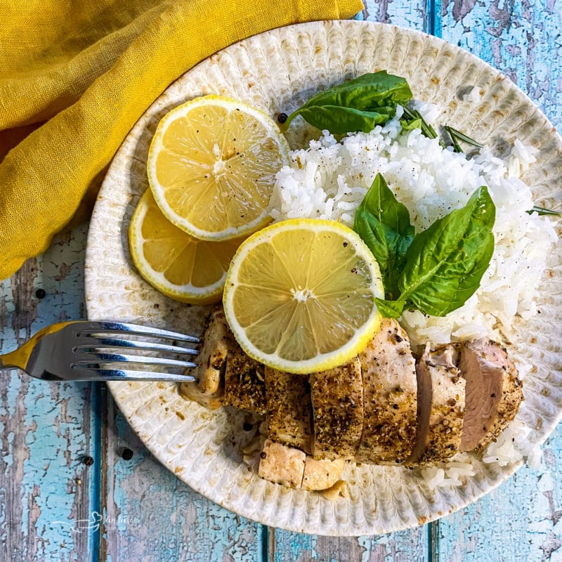 one plate with lemon pepper chicken, lemons, rice, and basil