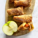 Air Fryer Apple Pie Egg Rolls and half an apple on a wood board