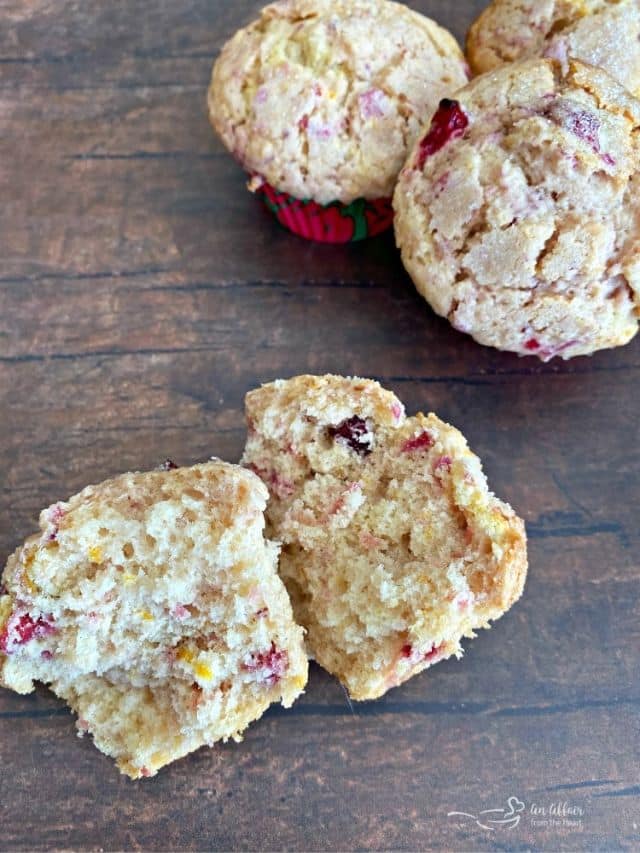 A cranberry orange muffin cut in half on a wood surface.