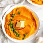 Instant Pot Sweet Potato Mash topped with parsley and butter in a white serving bowl