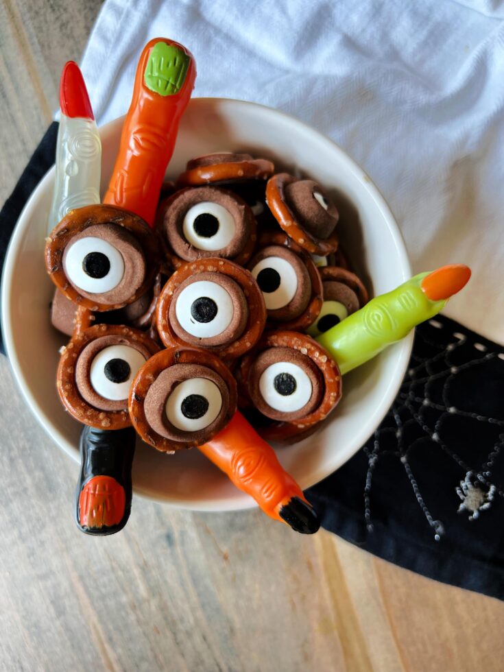 rolo pretzel eyeballs and plastic witches fingers in a white serving bowl.