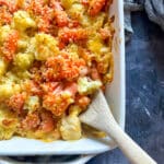 Cauliflower and Carrot Gratin and a wooden serving spoon in a white baking dish close up.