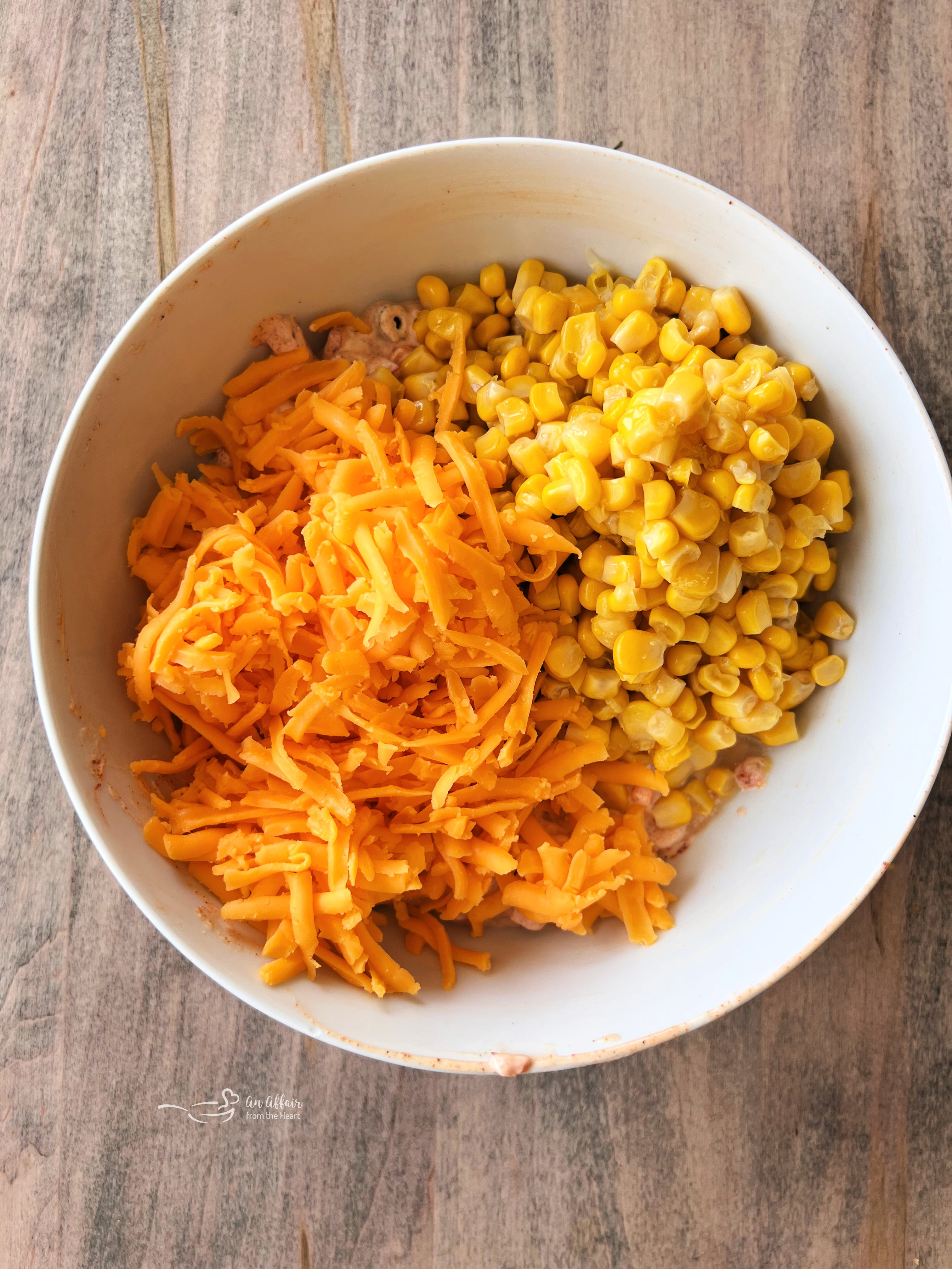 Fiesta Frito Corn Salad 6 Step 2: Folding in drained corn kernels and shredded cheddar cheese into the creamy dressing