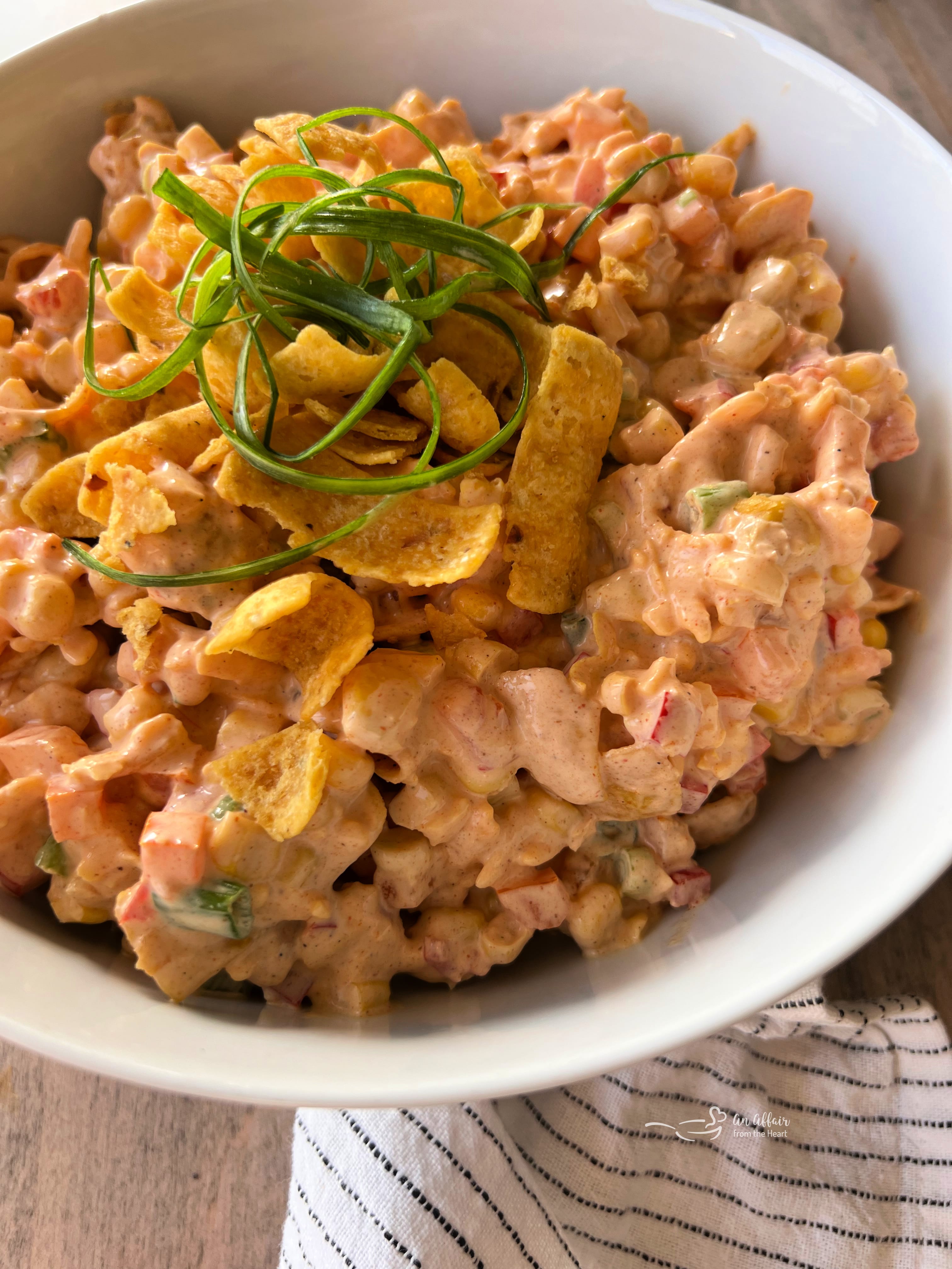 Fiesta Frito Corn Salad 4 Ingredients for Frito Corn Salad laid out on a white surface: corn, bell peppers, green onions, mayonnaise, sour cream, cheese, taco seasoning, and Fritos