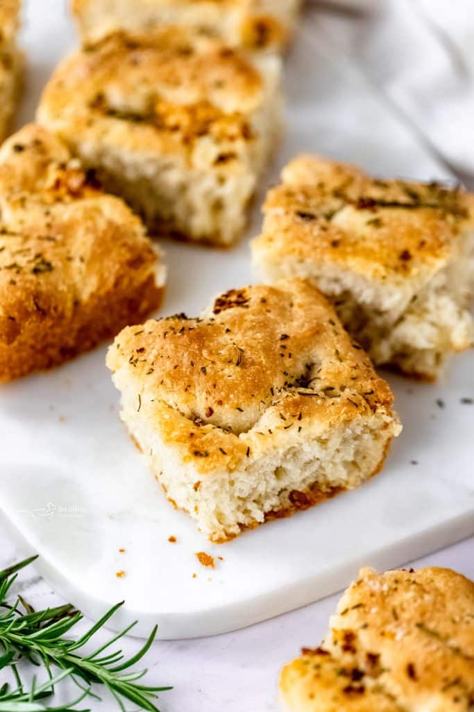 Close up of pieces of the garlic rosemary focaccia on a white serving plate