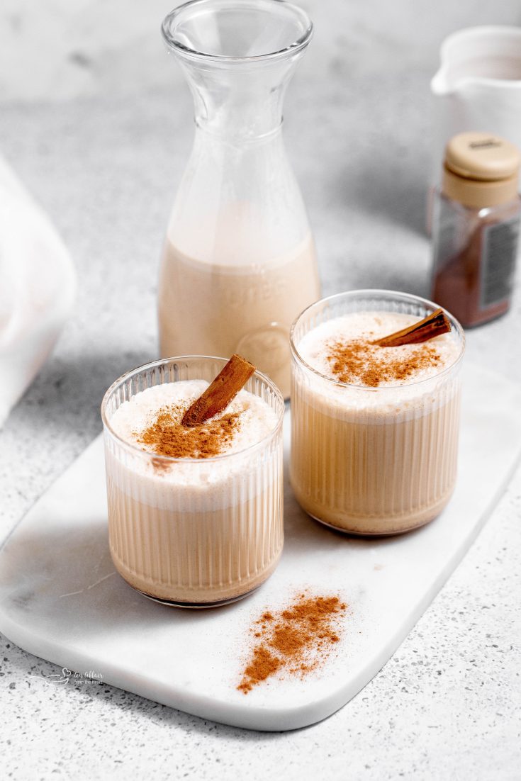 Two glasses of eggnog topped with a cinnamon stick.
