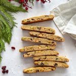 Holiday biscotti on a white surface with pine tree and berries around it.