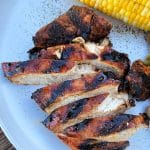 Sliced Sweet & Smoky Chicken and an ear of corn on a white plate.
