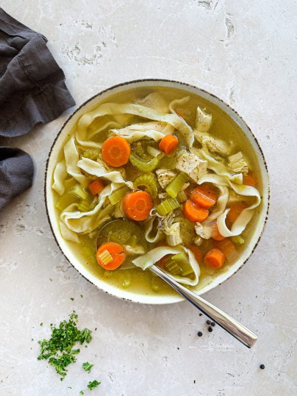 Close up of Homemade Chicken Noodle Soup and a spoon in a white bowl.