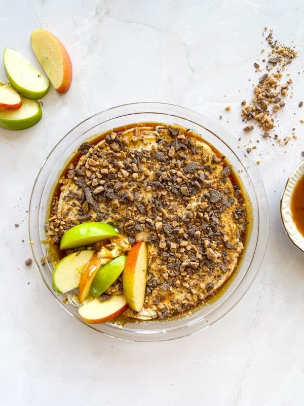 Caramel apple dip with slices of apples in it.