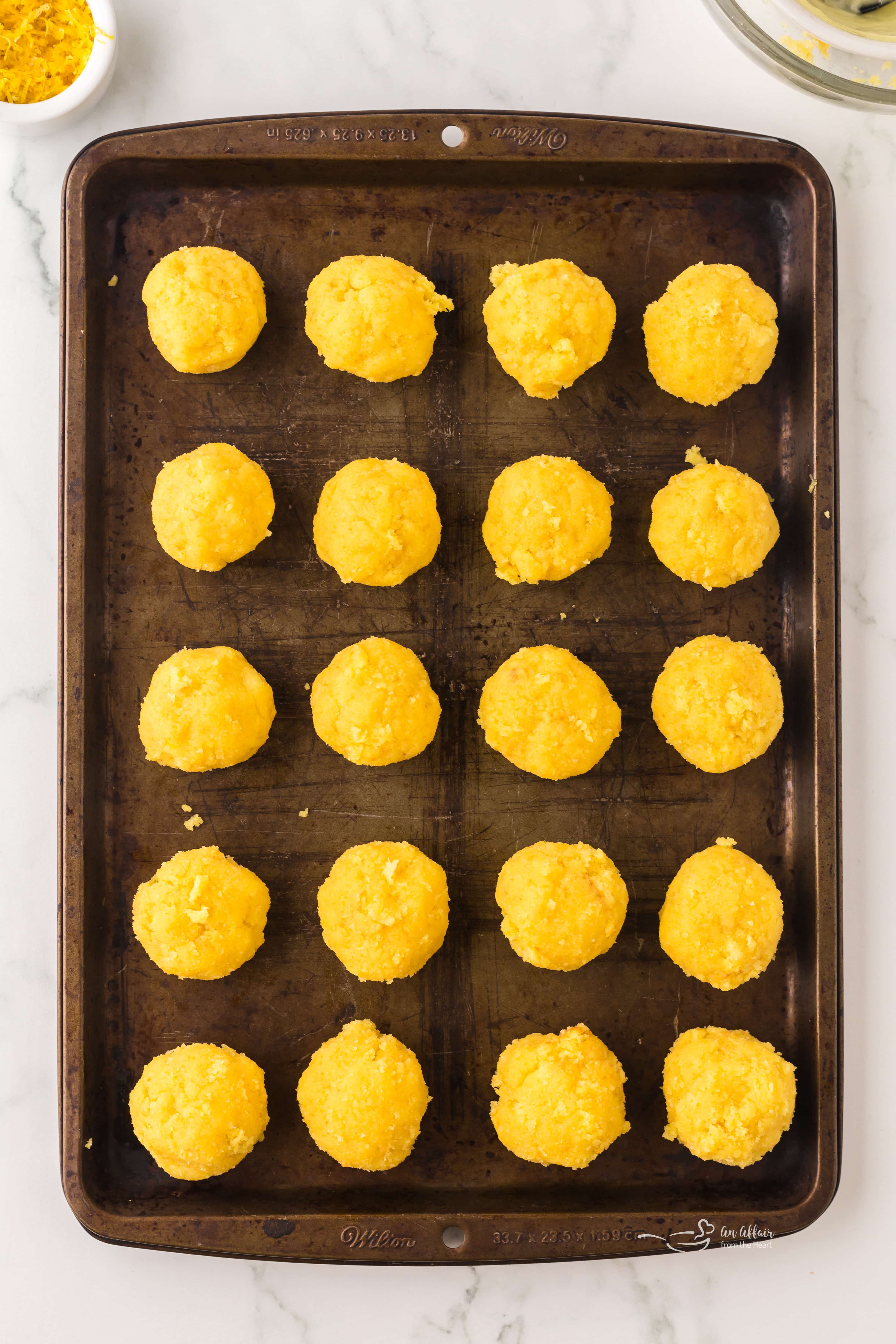 Hands rolling the lemon cake and frosting mixture into uniform truffle balls, placed on a baking sheet.