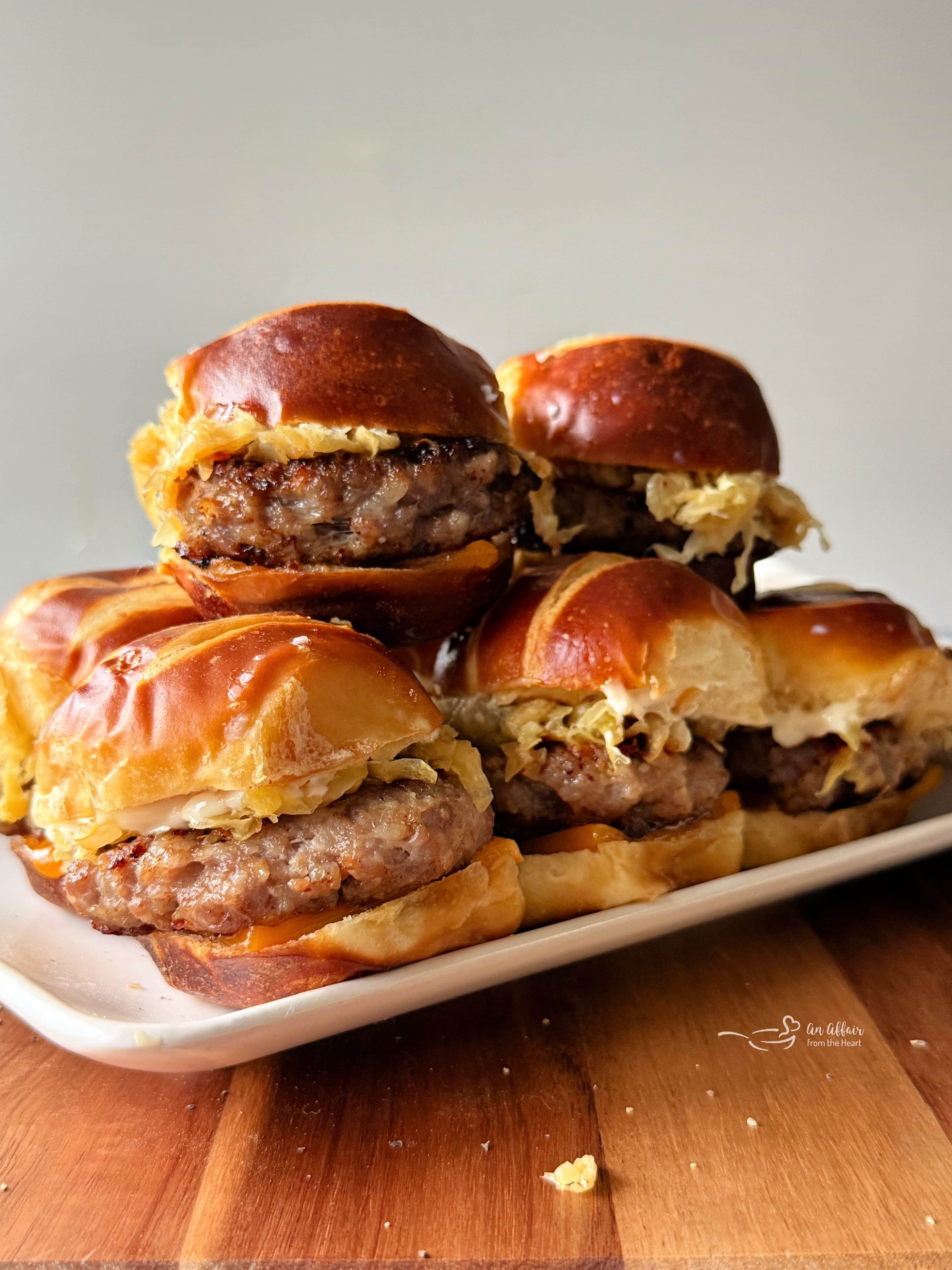 Bratwurst Sliders stacked on a white serving platter.